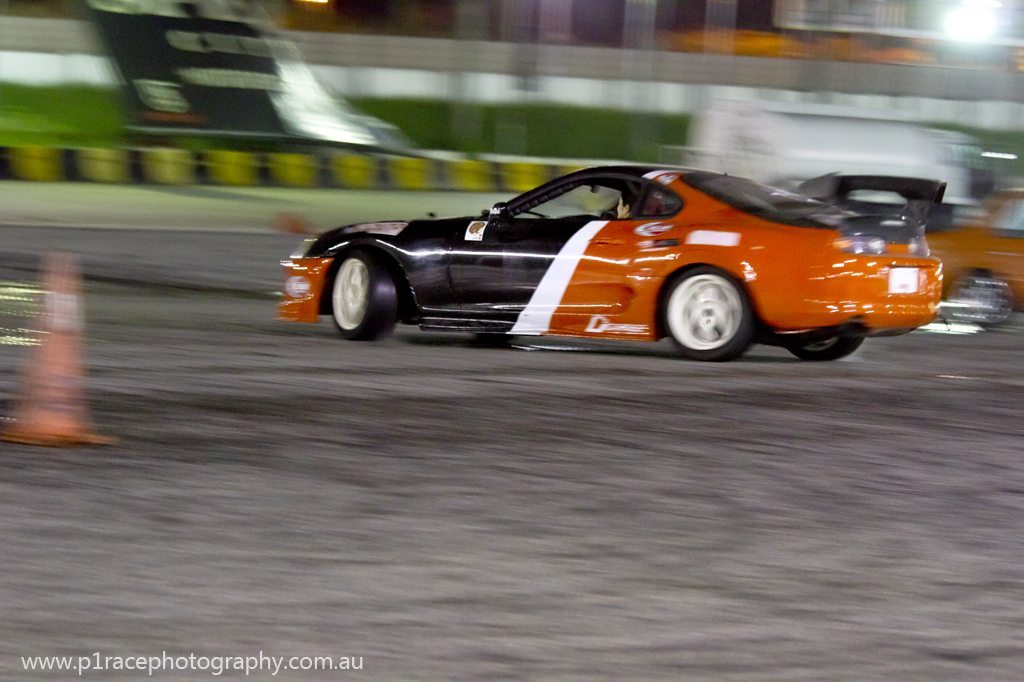 Speed City drift night - Orange and black Toyota Supra - Kazuto Garage - rear three-quarter pan 1 - Anna inside 5