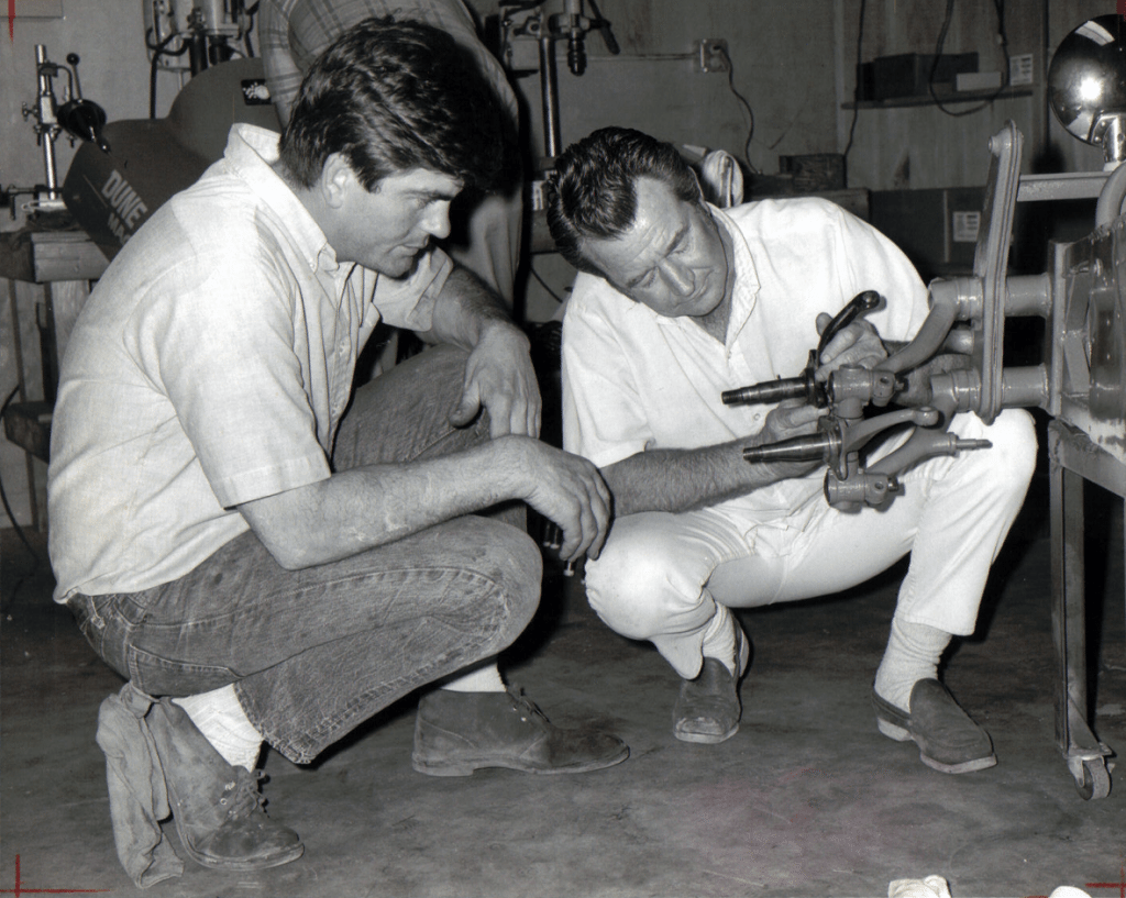 Always at home within the confines of his work shop, Drino Miller (left) and one-time business partner Sanford Havens compare the thickness of a Porsche 356 spindle (bottom) to a stock VW production unit in this early publicity photo.  The duo introduced the highly popular fiberglass VW "Baja Bug" kit to the world in the late 1960s.   